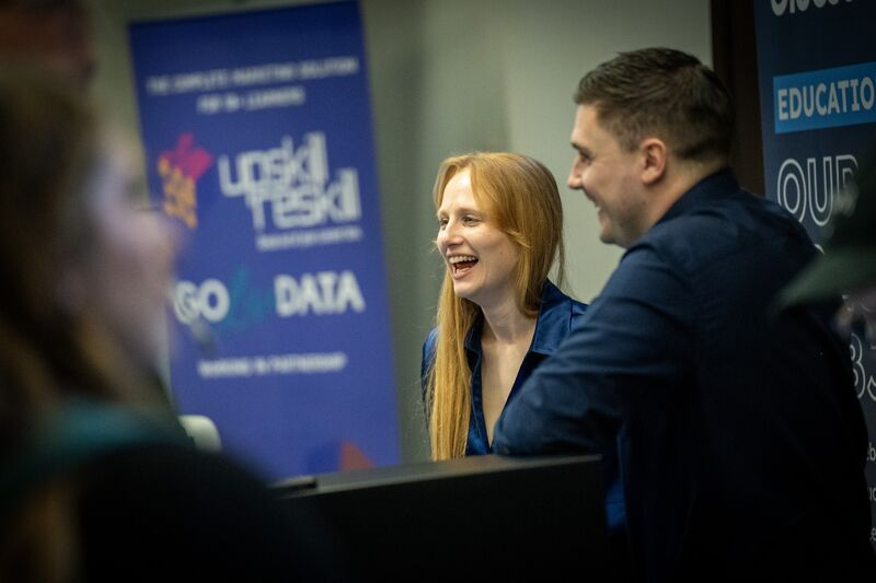 Two Bluestorm colleagues laughing while talking to somebody at an exhibition stand 
